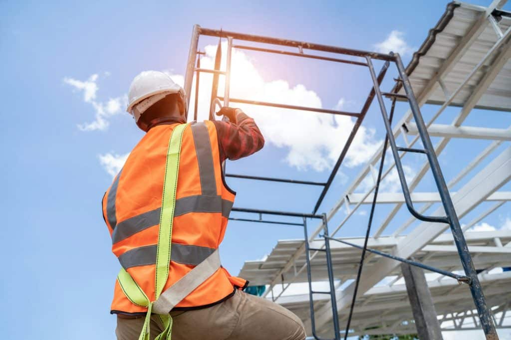 Construction worker wearing safety harness and safety line with tools are climbing scaffolding.