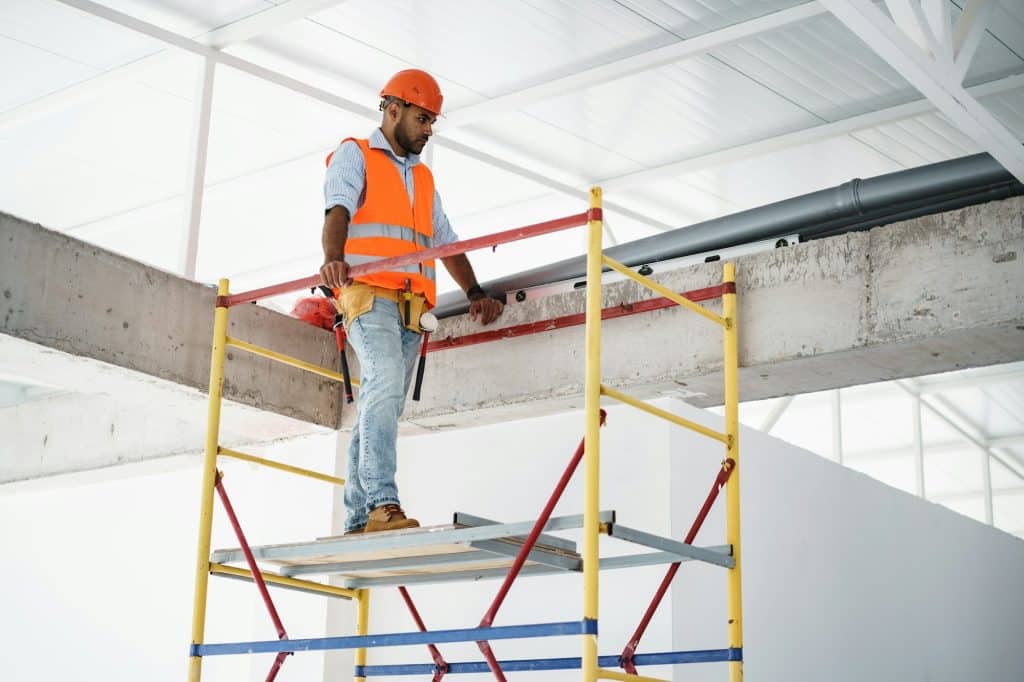 Young handsome builder climbing on scaffolding at construction site